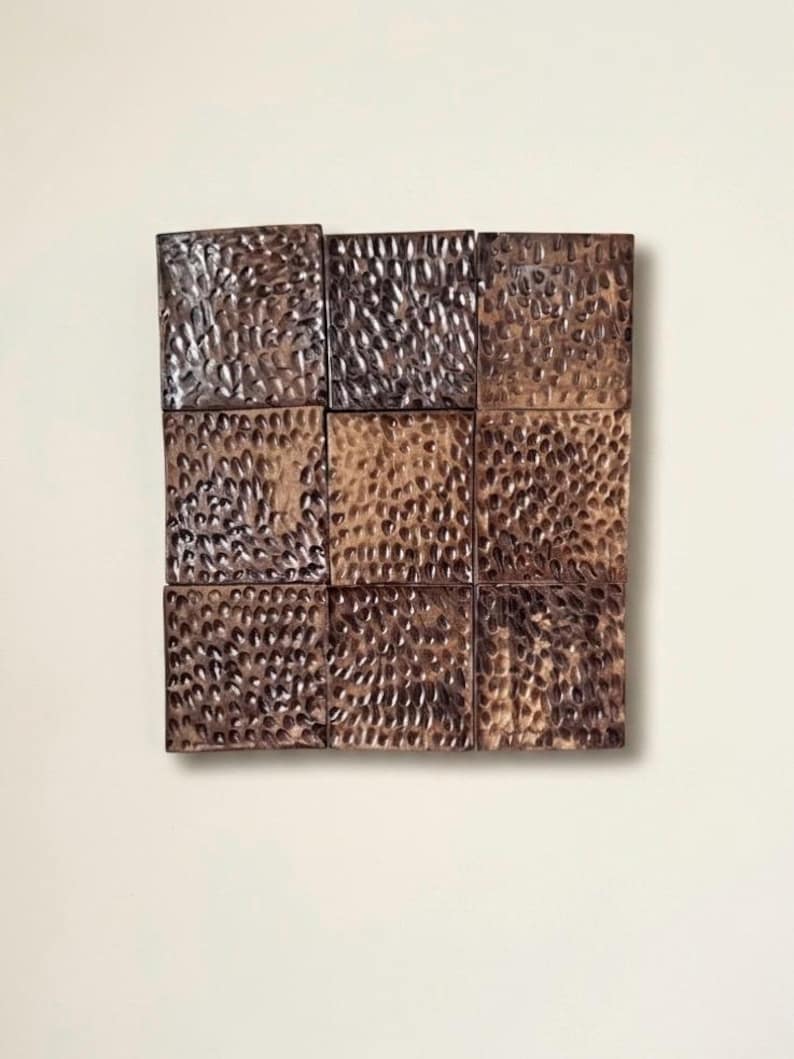 May include: A square wall art piece composed of nine individual square tiles arranged in a three-by-three grid. Each tile features a dark brown finish with a deeply hammered, textured surface that creates a repeating pattern of small indentations.