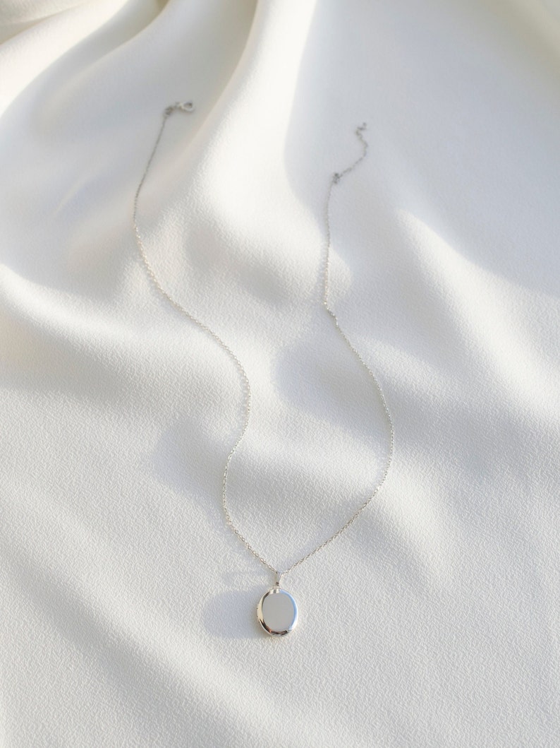 Pu&ograve; includere: Una collana d'argento con un ciondolo rotondo. Il ciondolo &egrave; liscio e riflettente, appeso a una catena delicata. La collana &egrave; presentata su un tessuto bianco strutturato, creando un'estetica minimalista. Il gioiello &egrave; semplice ed elegante.