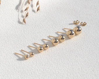 May include: A set of gold ball stud earrings of varying sizes. The earrings are arranged in a line from largest to smallest.