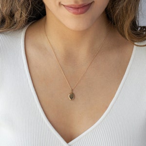 Pu&ograve; includere: Una collana con pendente a medaglione ovale color oro. La collana ha una catena delicata e un piccolo medaglione di forma ovale. Il medaglione &egrave; sospeso alla catena ed &egrave; centrato su un top bianco.