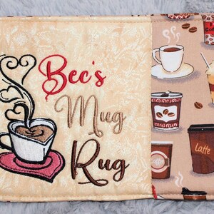 May include: A beige and brown fabric mug rug with the text "Bec's Mug Rug" embroidered on one side. The other side features a repeating pattern of coffee cups, coffee beans, and the words "latte" and "hot".