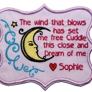May include: A lavender embroidered patch with a scalloped edge. The patch features a crescent moon with a face, text that reads "The wind that blows has set me free Cuddle this close and Dream of me Sophie", a star, and decorative swirls.