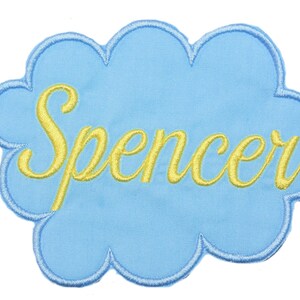 May include: A light blue cloud-shaped patch with the name "Spencer" embroidered in yellow thread.