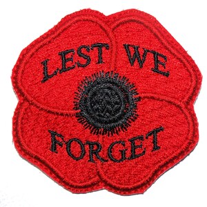 May include: A red poppy flower patch with the words "LEST WE FORGET" embroidered in black. The centre of the poppy is black, and the petals are red. This patch is designed to be sewn onto clothing or accessories.