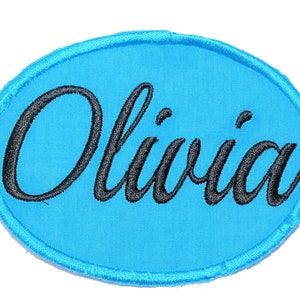 May include: A blue oval-shaped patch with the name "Olivia" embroidered in black cursive lettering.