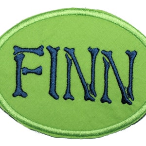 May include: Green oval-shaped patch with a white outline. The word "FINN" is embroidered in blue with a bone-like design.