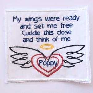 May include: White fabric patch with embroidered text "My wings were ready and set me free Cuddle this close and think of me" and a red heart with the word "Poppy" inside, surrounded by black wings.