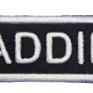 May include: White embroidered patch with a black background and the name "ADDIE" in white lettering.