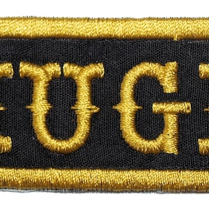 May include: Gold embroidered name patch with the name "HUGH" on a black background.