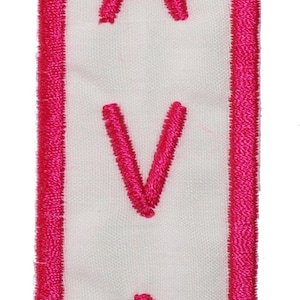 May include: A pink embroidered patch with a white background and the name "AVA" in pink lettering.