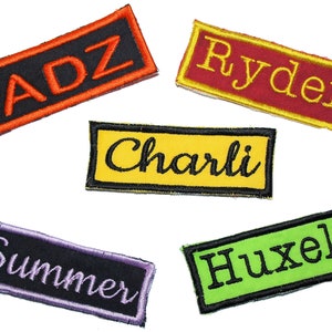 May include: Five embroidered fabric patches with different names: ADZ, Ryder, Charli, Summer, and Huxely. The patches are rectangular and have black outlines. The names are embroidered in different colours: orange, yellow, gold, purple, and green.