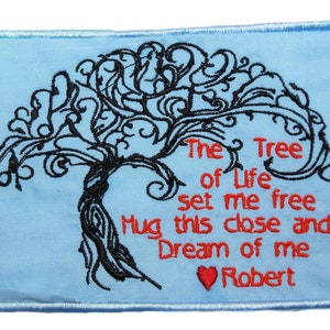 May include: Embroidered patch featuring a black tree design on a pale blue backdrop. The text "The Tree of Life set me free Hug this close and Dream of me Robert" is in red. A red heart is at the bottom.