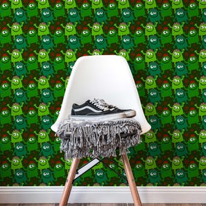 May include: A white chair with wooden legs supports a grey fringed blanket and a black and white trainer. The background features a repeating pattern of green cartoon monsters with red accents.