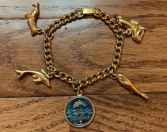 Pulsera con dijes SeaWorld de 1976, cadena dorada de 15 cm, 5 dijes: delfín, morsa, ballena, león marino, medallón con el logotipo de Orlando, cierre plegable.