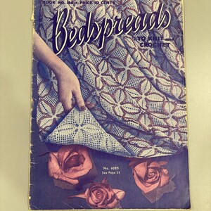 May include: Vintage book cover titled "Bedspreads To Knit and Crochet." The cover features a detailed pattern of a bedspread in shades of blue and brown, with a hand holding up a corner. Pink roses are at the bottom.