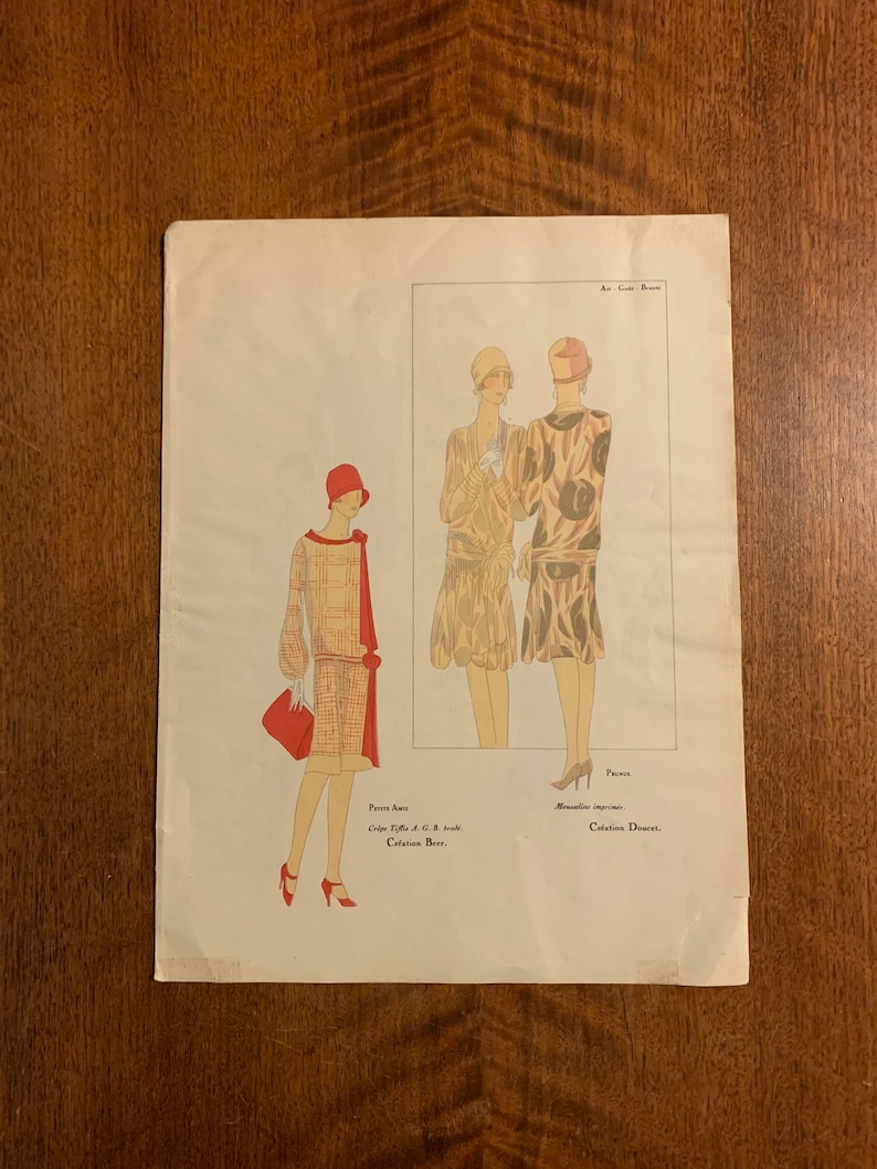 May include: A vintage fashion illustration from the 1920s featuring three women wearing dresses and hats. The illustration is in black and white with red accents. The text on the page reads "Paris, Crepe Tulle, A.C.B. Jouvin, Creation Beer,  Monalune Imprime, Collection Doucet."