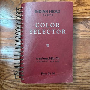 May include: A red spiral bound book with the title "INDIAN HEAD CLOTH COLOR SELECTOR" and the text "Nashua Mfg. Co. 40 WORTH ST., NEW YORK" and "Price $1.50".