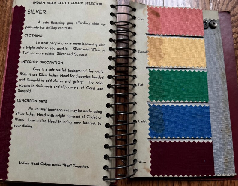 May include: A page from a fabric color guide book showing swatches of different colors. The colors are labeled with names like "Coral", "Sungold", "Turf", "Cadet", and "Wine". The text on the page says "Indian Head Cloth Color Selector" and "Indian Head Colors never "Run" Together."