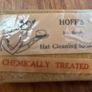 May include: A rectangular hat cleaning sponge in a clear plastic wrapper. The label reads "HOFF'S Mt. Horeb Hat Cleaning Sponge" with a drawing of a person holding a hat. The bottom label says "CHEMICALLY TREATED".