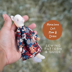 May include: A small fabric cat doll wearing a long-sleeved dress with a dark blue, red, and white floral pattern. Text on the image reads: Miniature Cat Mum & Dress SEWING PATTERN & GUIDE. The doll has a white head and light-colored limbs.