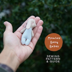 Può includere: Una piccola bambola coniglio in tessuto beige con una salopette azzurra. Il testo sull'immagine recita Miniature Bunny Babies SEWING PATTERN & GUIDE. Il coniglio ha orecchie lunghe e un viso cucito semplice, presentato come progetto di cucito.