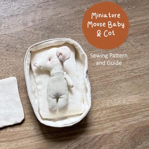 Könnte beinhalten: Eine Miniatur-Stoffpuppe in Form eines Mäusebabys, das in einem ovalen Stoffbettchen liegt, begleitet von einem separaten quadratischen Stoffstück. Der Text Miniature Mouse Baby & Cot Sewing Pattern and Guide ist oben rechts sichtbar.