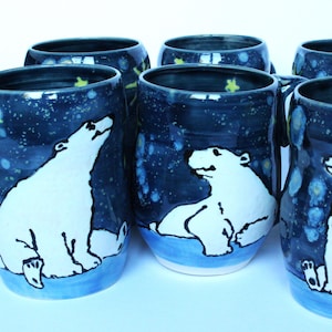May include: Six blue ceramic mugs featuring white polar bear illustrations and a starry night sky design. Each mug has a different polar bear pose.