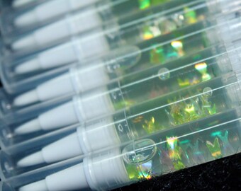 May include: Close-up of several clear, pen-shaped containers with white tips. The containers are filled with a clear liquid and iridescent glitter. The pens are arranged in a diagonal row, with the tips facing the same direction.
