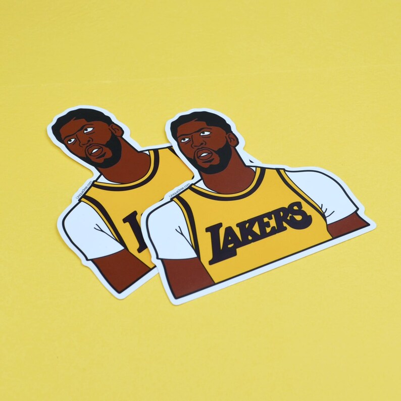 Puede incluir: Dos pegatinas de un jugador de baloncesto que lleva una camiseta amarilla con la palabra "LAKERS" en la parte delantera. El jugador mira hacia la derecha y tiene una expresi&oacute;n seria en su rostro.