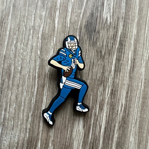 May include: A blue and white football player figurine running with a football in hand. The figurine is made of rubber and has a black base.