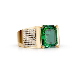 May include: A gold ring featuring a large, rectangular, emerald-cut green gemstone set in the center. The band is accented with multiple rows of small, clear, round-cut white stones embedded along the side of the gold metal shank.