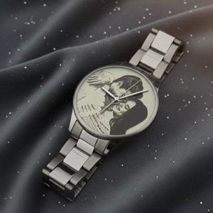 K&ouml;nnte beinhalten: Silberfarbene Armbanduhr mit einem Schwarz-Wei&szlig;-Foto eines Paares auf dem Zifferblatt. Die Uhr hat ein Metallarmband und ein rundes Zifferblatt. Das Foto zeigt ein sich umarmendes Paar.