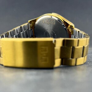 May include: A gold-toned wristwatch with a silver band is displayed against a dark background. The watch face is visible, with the date "4.15.23" engraved on the back. The watch band is a combination of gold and silver links.
