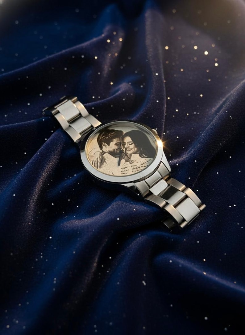 May include: A silver wristwatch with a stainless steel band. The watch face features a black and white photograph of a couple. The watch is displayed on a dark blue, textured surface with small, white, sparkling accents.