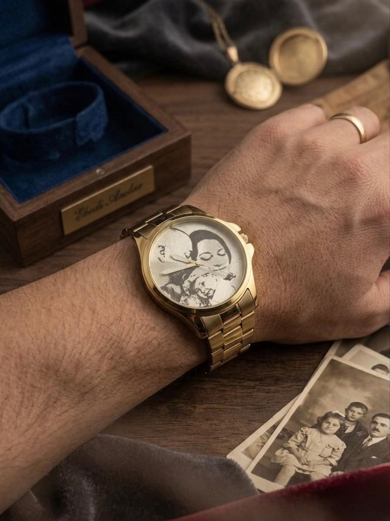 Puede incluir: Un reloj de pulsera dorado con una imagen grabada personalizada en la esfera. El reloj est&aacute; en una mu&ntilde;eca, con una correa dorada y una esfera rectangular. Una caja de madera y fotograf&iacute;as antiguas est&aacute;n en el fondo.