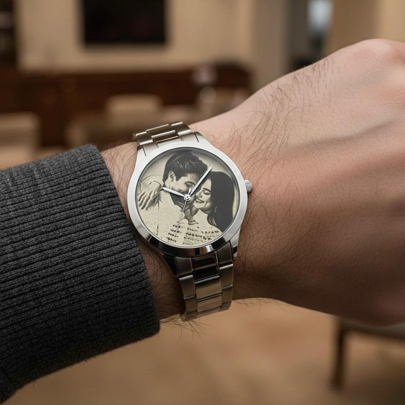 May include: Silver wristwatch with a stainless steel band. The watch face features a black and white image of a couple embracing. The watch is on a person's wrist, with a gray sweater sleeve visible.