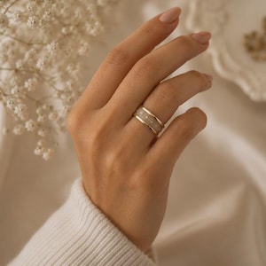 May include: A wide band ring featuring a central inlay of translucent, light-colored material framed by two thin gold-toned edges. The center inlay is punctuated by a series of small, evenly spaced circular metallic accents along its circumference.