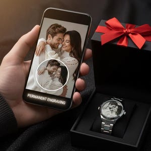May include: A silver wristwatch with a photo of a couple inside a black gift box with a red bow. A smartphone displays the same photo with the text "PERMANENT ENGRAVING". The watch is on a silver metal band.