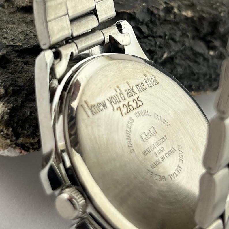 May include: Silver stainless steel watch with a rectangular face and a metal band. The watch back is engraved with the text "I knew you'd ask me that 7.26.25". The watch is water resistant and made in China.