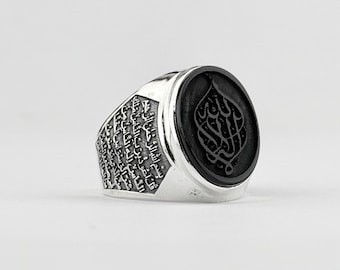May include: A silver ring with a black onyx stone featuring Arabic calligraphy. The band of the ring is engraved with Arabic script.