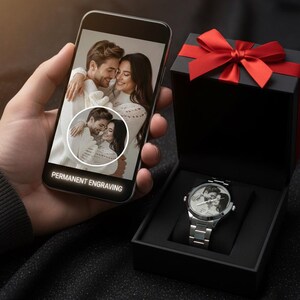 K&ouml;nnte beinhalten: Eine silberne Armbanduhr mit einem auf dem Zifferblatt eingravierten Foto, pr&auml;sentiert in einer schwarzen Geschenkbox mit roter Schleife. Ein Smartphone zeigt dasselbe Foto mit dem Text "PERMANENT ENGRAVING". Der Markenname "TarikMasterJewelry" ist sichtbar.