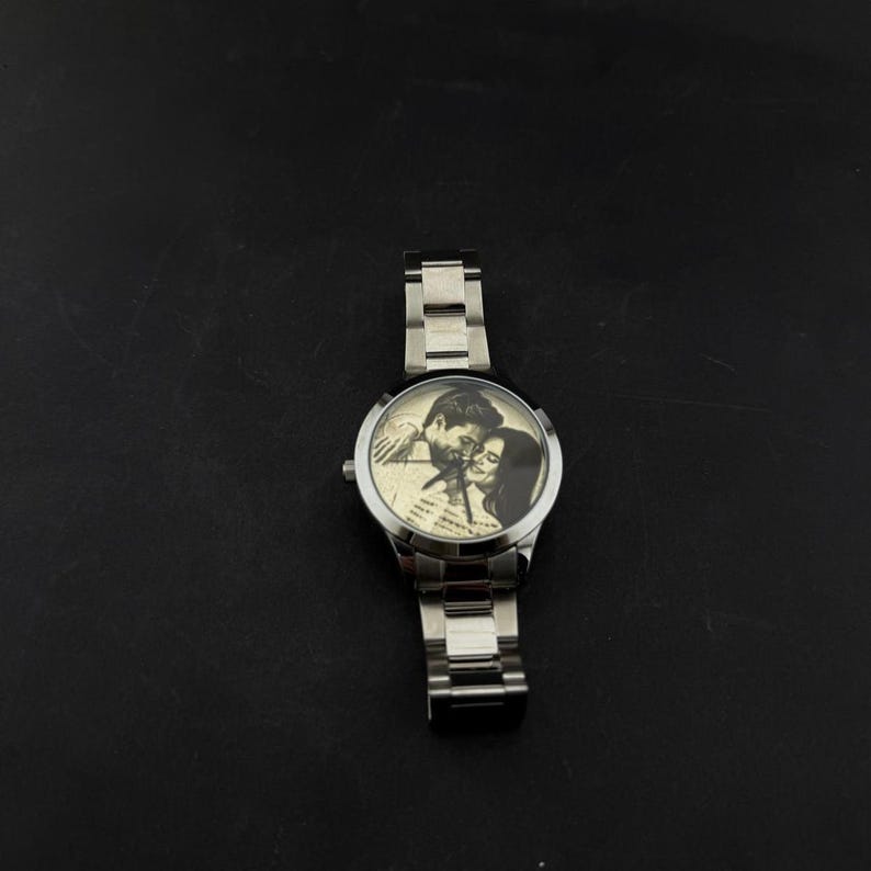 May include: A silver wristwatch with a stainless steel band. The watch face features a black and white image of a couple. The watch is a classic design, suitable for everyday wear.