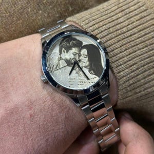 May include: A silver wristwatch with a stainless steel band. The watch face features a black and white image of a couple. The watch is on a wrist.