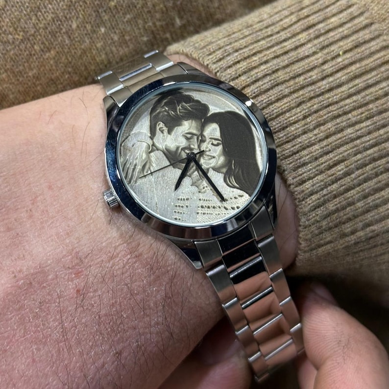 May include: A silver wristwatch with a stainless steel band. The watch face features a black and white image of a couple. The watch is on a wrist.