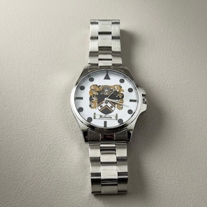 May include: A silver wristwatch with a white face featuring a family crest design. The watch has a stainless steel band and a round face with black markers and the name "Roberts" below the crest. The watch is a classic accessory.