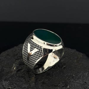 May include: A silver ring with a dark green oval gemstone set in a textured band.