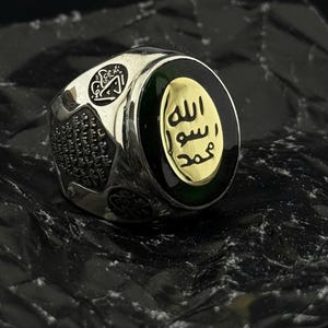 May include: A silver ring with a green and black stone featuring the Arabic text "Muhammad is the Messenger of Allah".