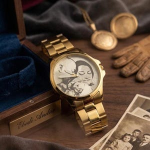 Puede incluir: Un reloj de pulsera dorado con una esfera personalizada que muestra una imagen en blanco y negro de una familia. El reloj se exhibe con una caja de madera, fotograf&iacute;as antiguas y un colgante dorado. La correa del reloj es de metal dorado.