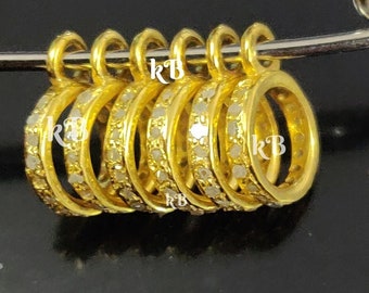 May include: Five gold rings with a row of small white stones around each ring. The rings are stacked on a safety pin.