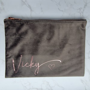 May include: A gray velvet zippered pouch with the name "Vicky" and a heart in rose gold lettering.